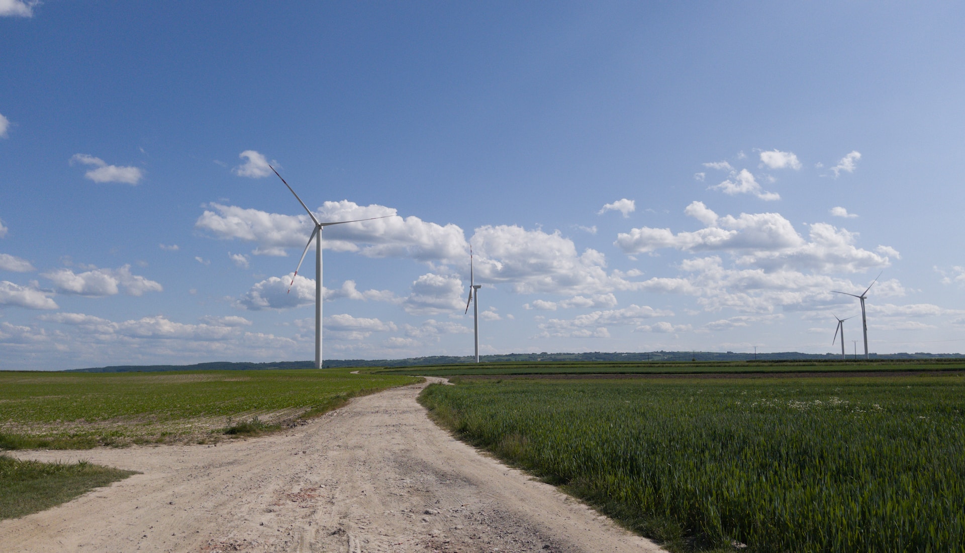 a dirt road going through a field with windmills in the background